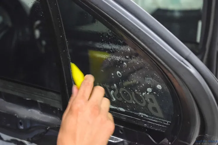 A person is cleaning a car window with a yellow sponge.