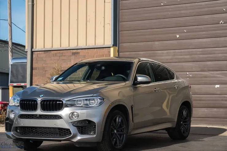 A silver bmw x6 m is parked in front of a garage door.