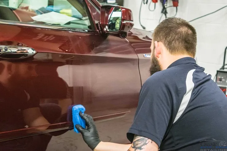 A man is polishing a red car with a blue sponge.