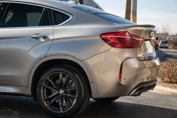 A silver bmw x4 m is parked on the side of the road.