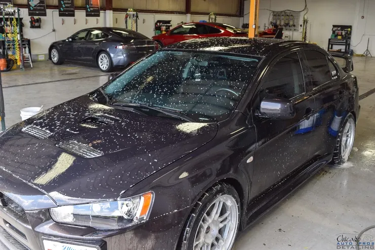 A black car is parked in a garage with other cars.