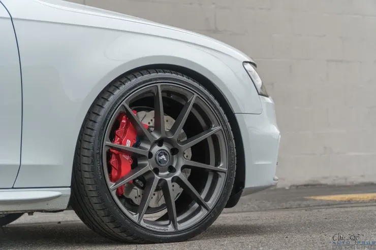 A white car with red brake calipers is parked in a parking lot.