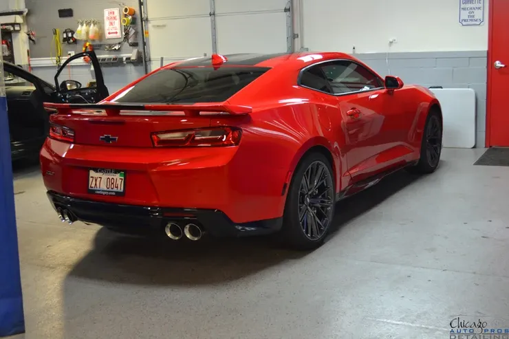 A red chevrolet camaro is parked in a garage