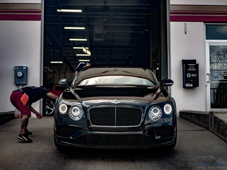 A man is bending over in front of a bentley car in a garage.