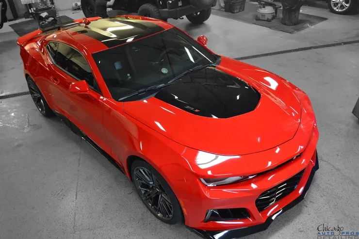 A red car with a black hood is parked in a garage