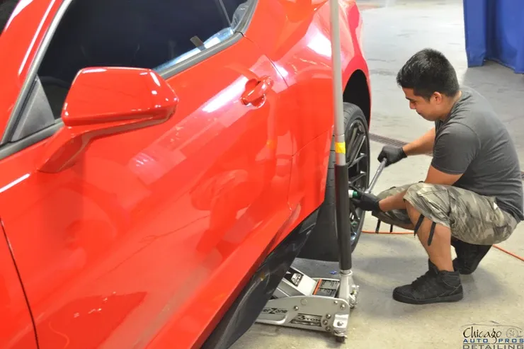 A man is changing a tire on a red car