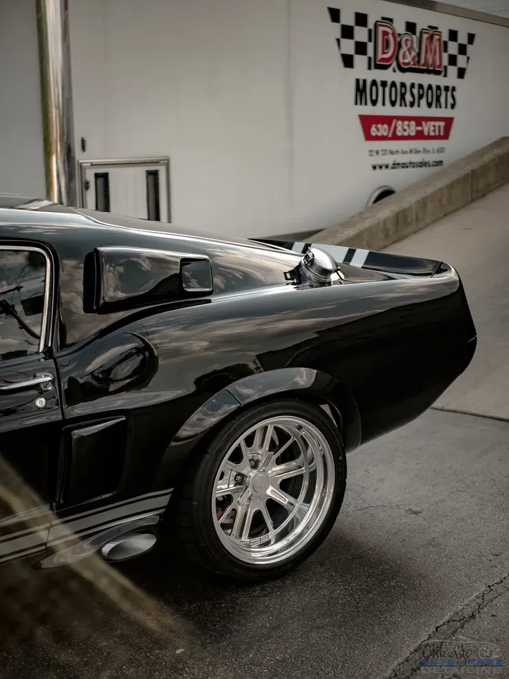 A black mustang is parked in front of a d & m motorsports trailer.