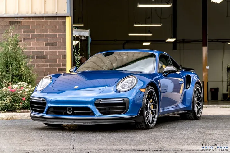 A blue porsche 911 turbo s is parked in front of a brick building.