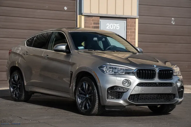 A silver bmw x6 m is parked in front of a garage.