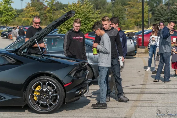 A group of people are standing around a black sports car with the hood up.
