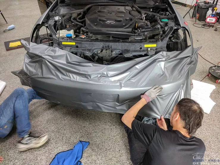 A man is wrapping a car with a piece of tape.