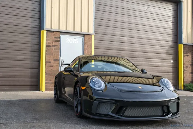 A black porsche 911 gt3 rs is parked in front of a garage door.