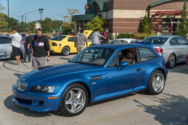 A blue bmw z3 is parked in a parking lot with other cars.