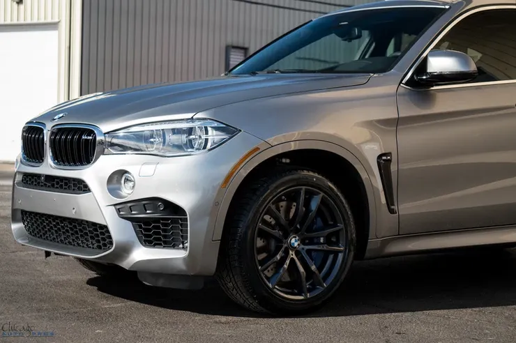 A silver bmw x6 m is parked in front of a garage.