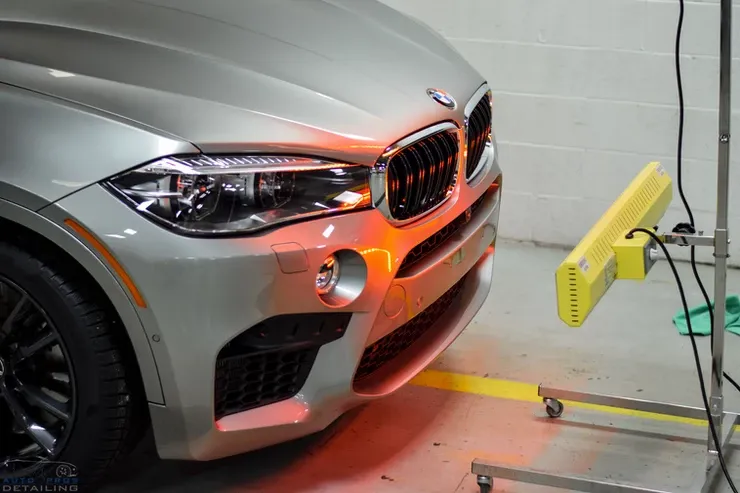 A silver bmw is sitting next to a yellow light.