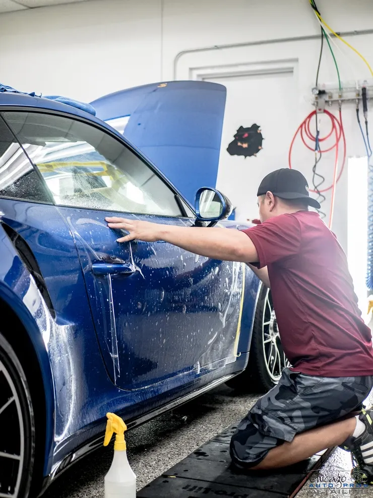 A man is kneeling down next to a blue car in a garage.