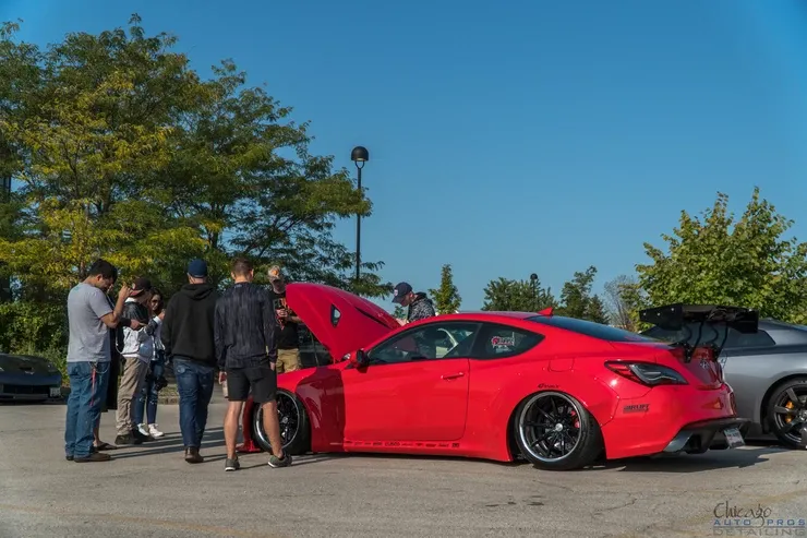 A group of people are standing around a red car with the hood up.