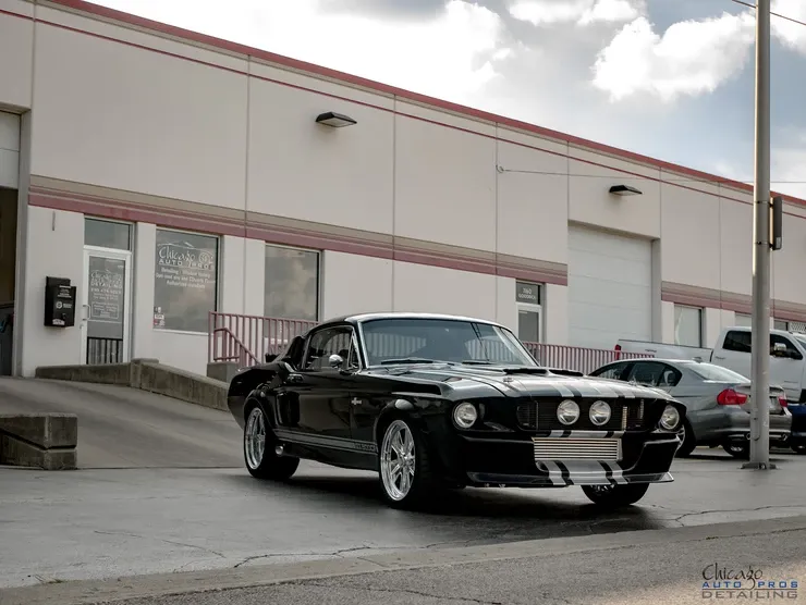 A black mustang is parked in front of a white building.