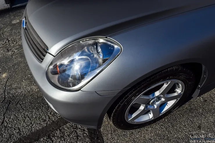 A close up of a silver car 's headlight and wheel