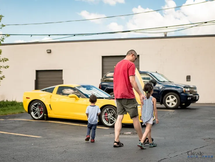A man and two children are walking in front of a yellow car