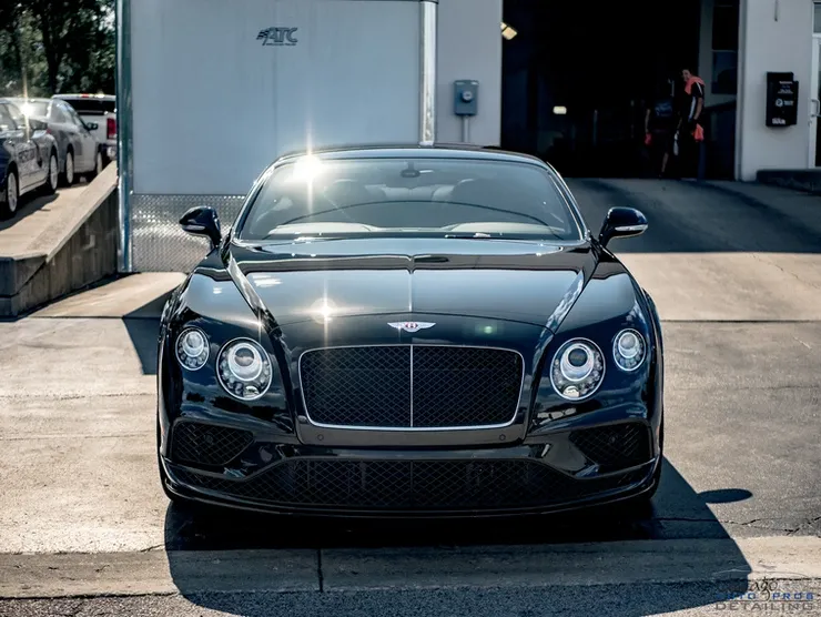 A black bentley is parked in front of a garage.