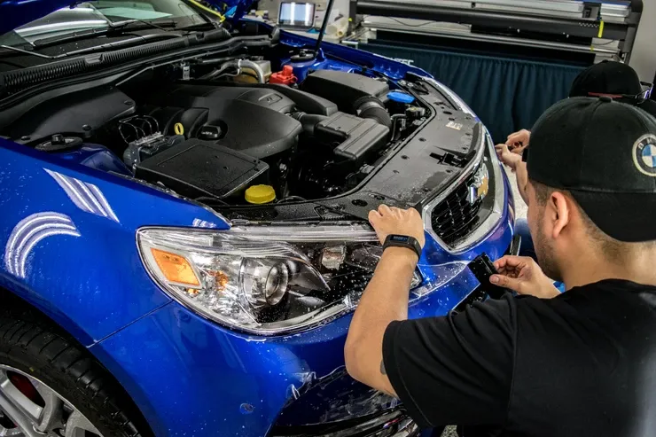 A man is applying a protective film to the front of a blue car.
