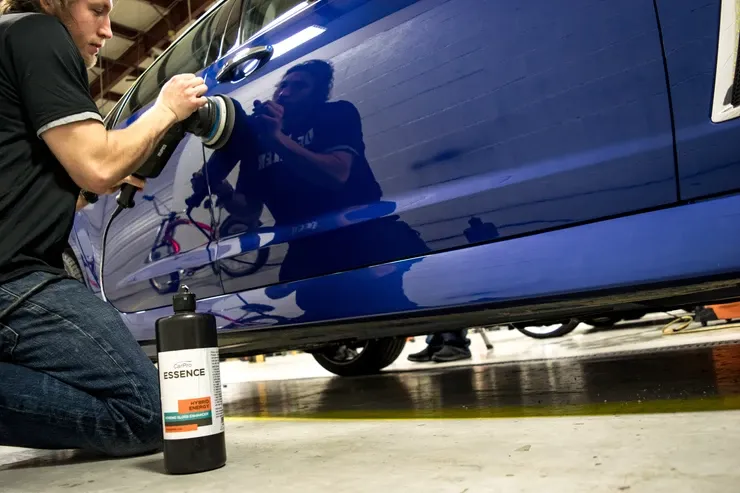 A man is kneeling down polishing a blue car in a garage.
