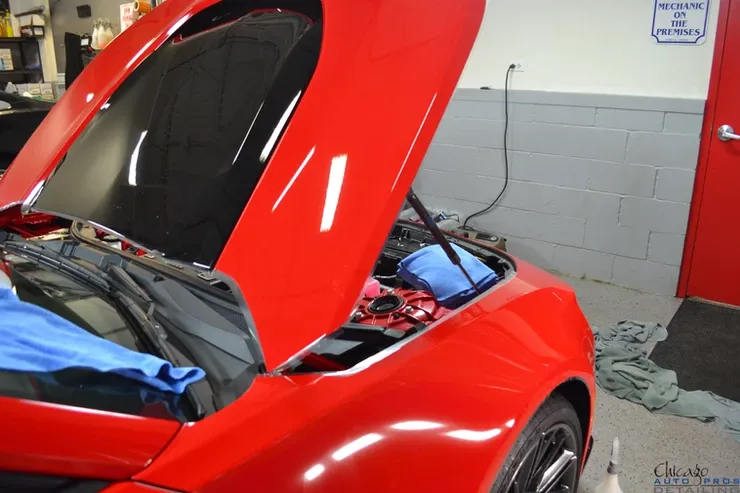 A red car with the hood up in a garage
