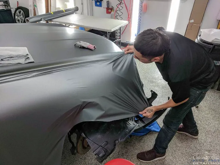 A man is wrapping a car in a black wrap in a garage.