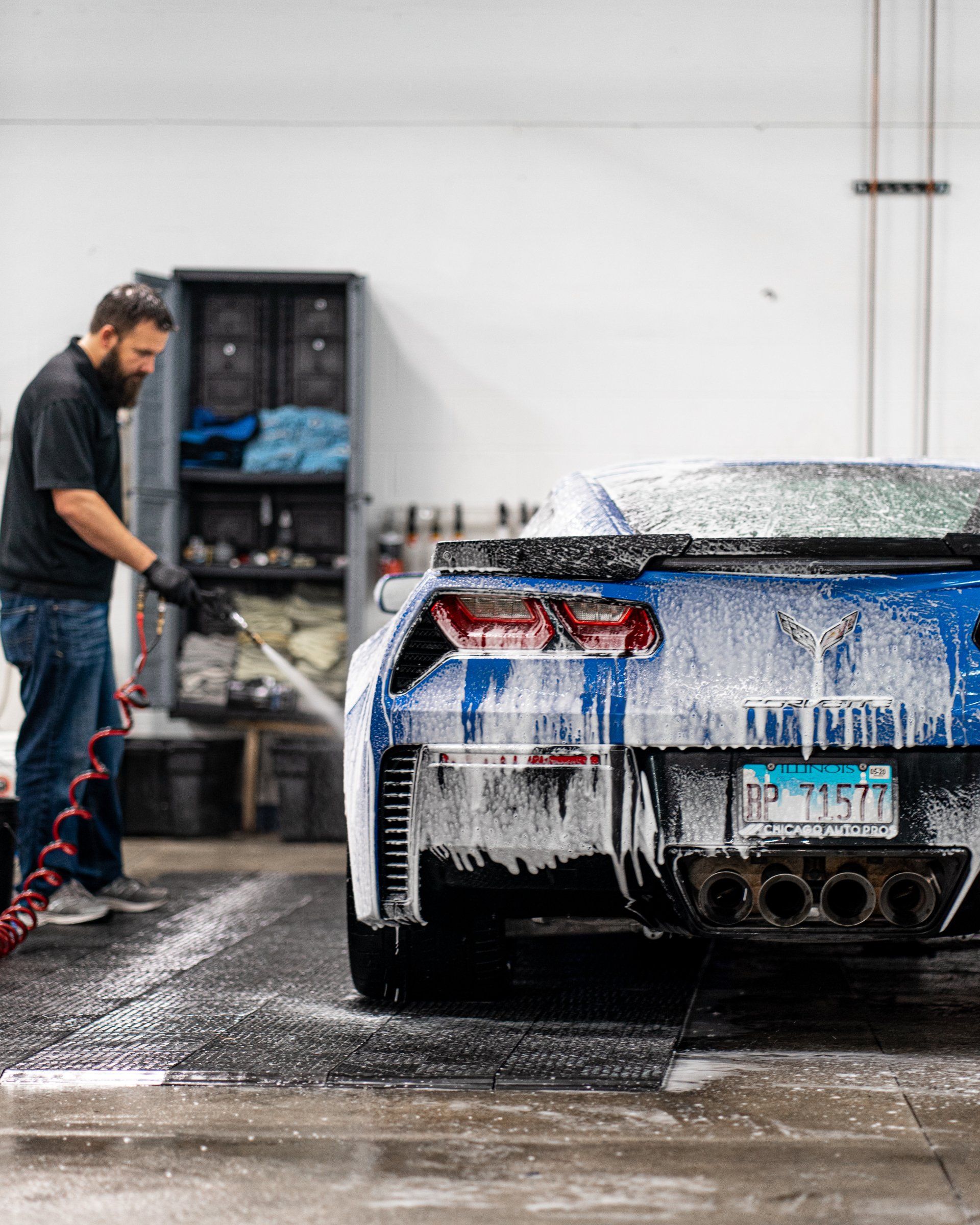 A man is washing a blue sports car in a garage.