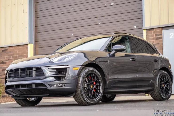A black porsche macan is parked in front of a garage door.