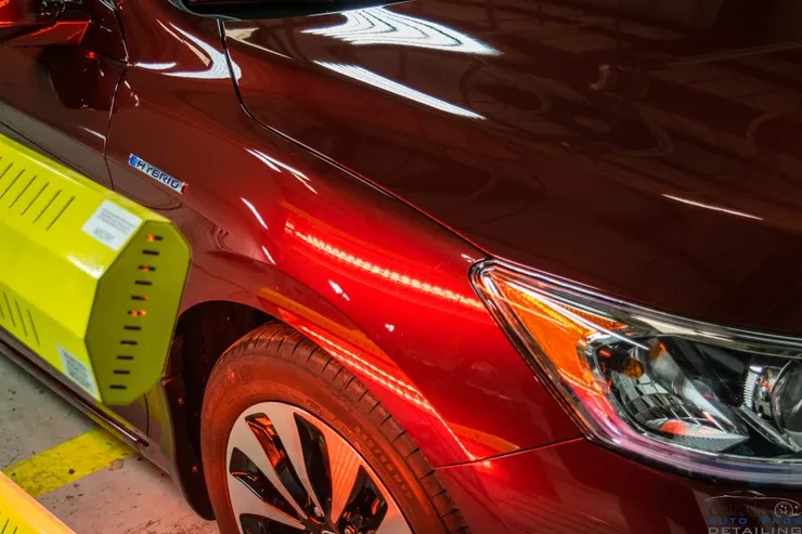 A red car is parked in a parking lot next to a yellow barrier.