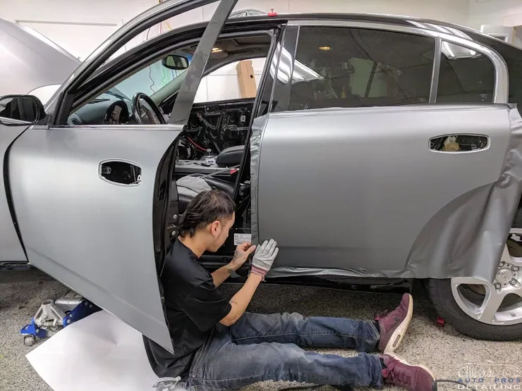 A man is sitting on the floor wrapping a car in a garage.