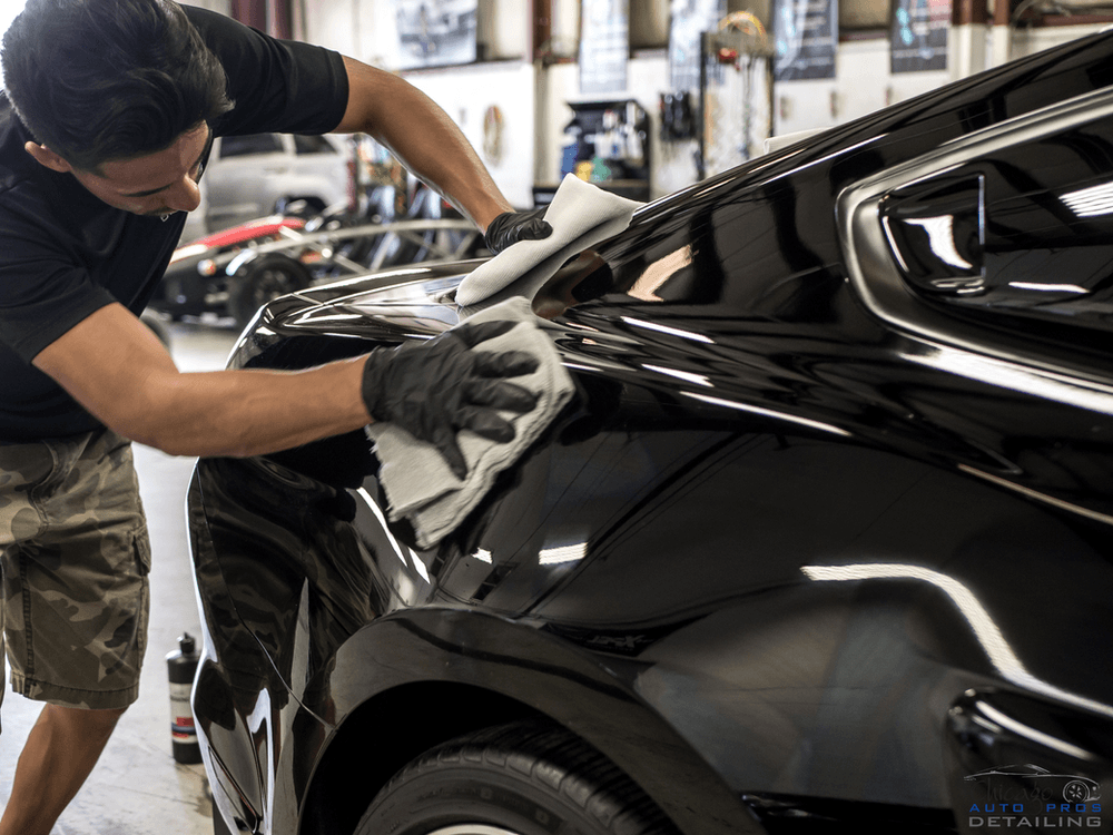A man is cleaning a black car with a cloth in a garage.