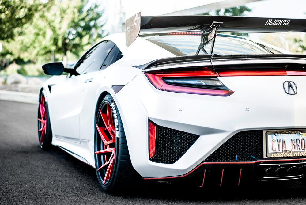 A white acura nsx with red wheels is parked on the side of the road.
