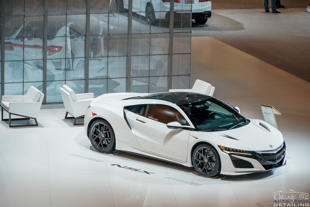 A white sports car is parked in front of a glass wall at a car show.