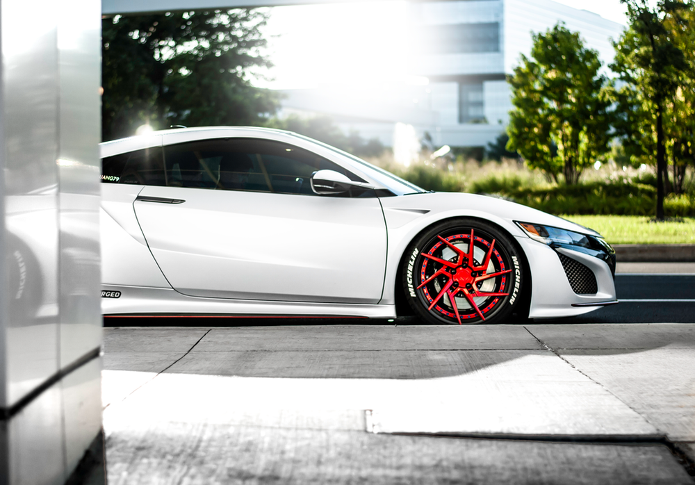 A white sports car with red wheels is parked on the side of the road.