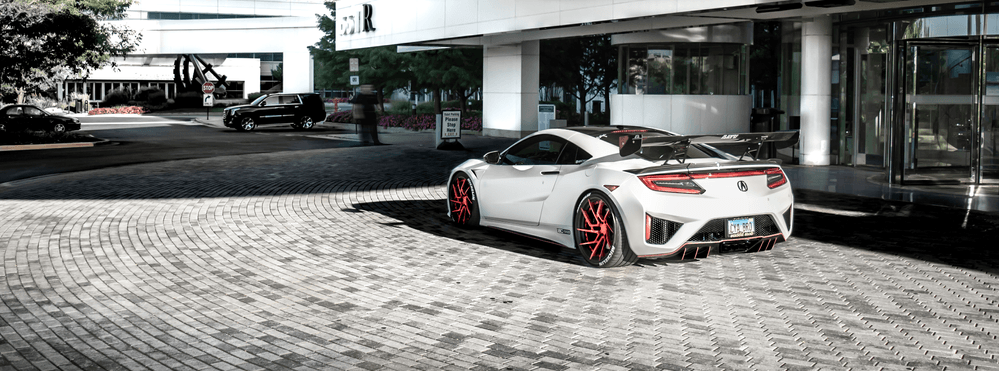 A white sports car is parked on a cobblestone driveway in front of a building.