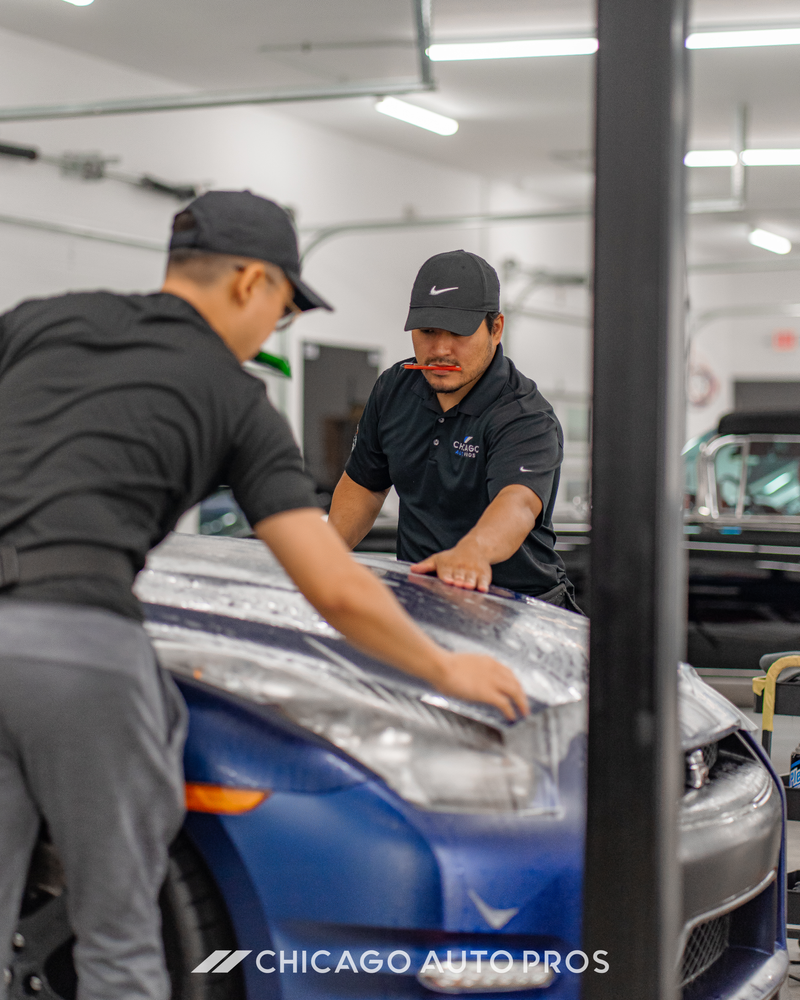 Two men are working on a blue car in a garage.