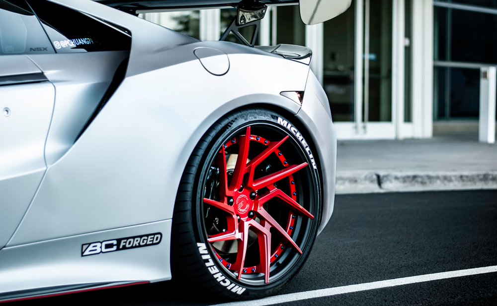 A silver sports car with red wheels is parked in a parking lot.