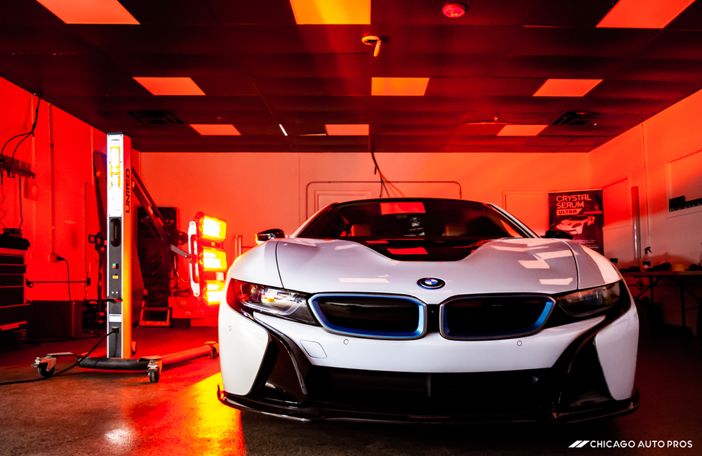 A white bmw i8 is parked in a garage with red lights.