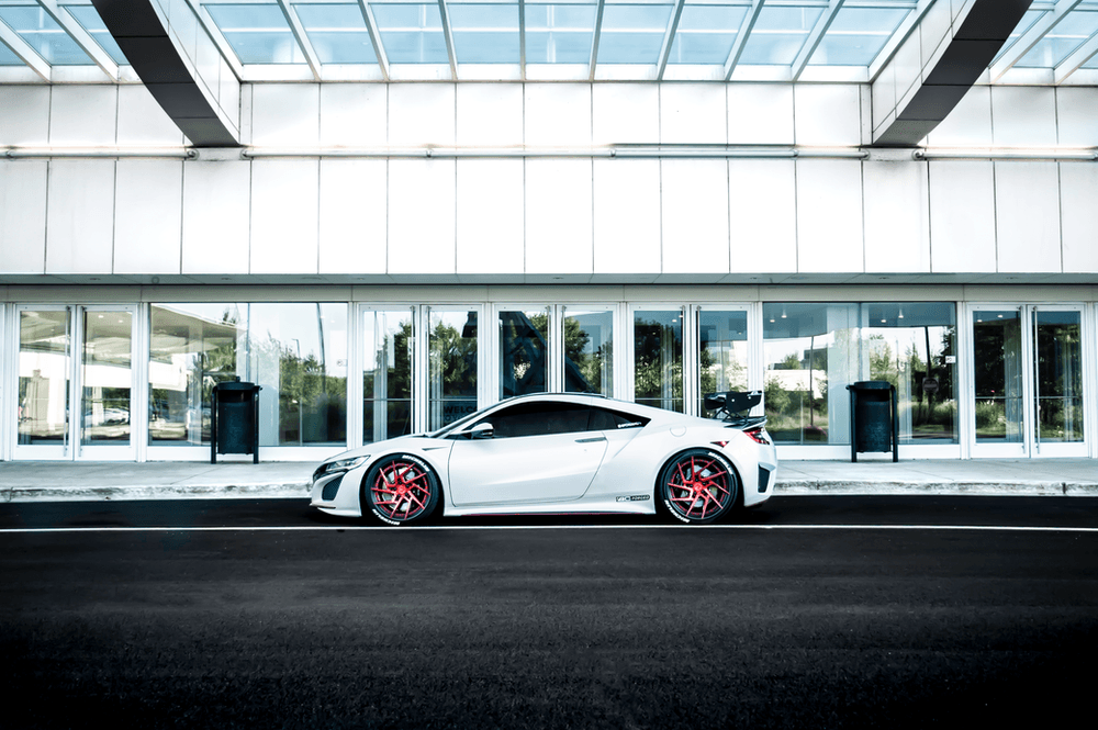 A white sports car is parked on the side of the road in front of a building.