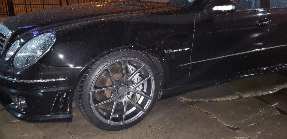 A black car with a broken tire is parked on the side of the road.