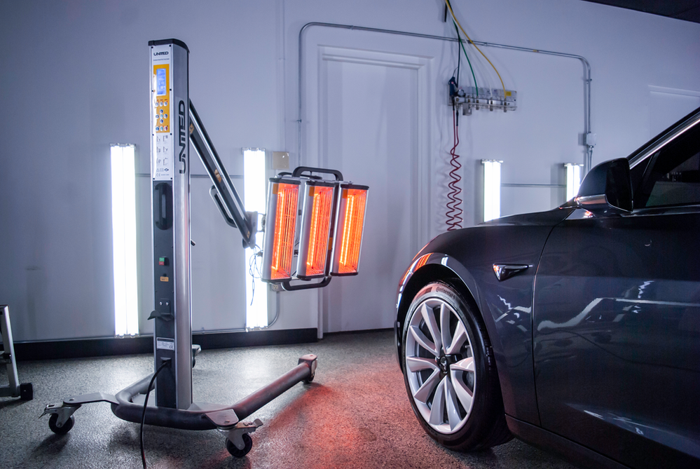A tesla model 3 is being painted in a garage.