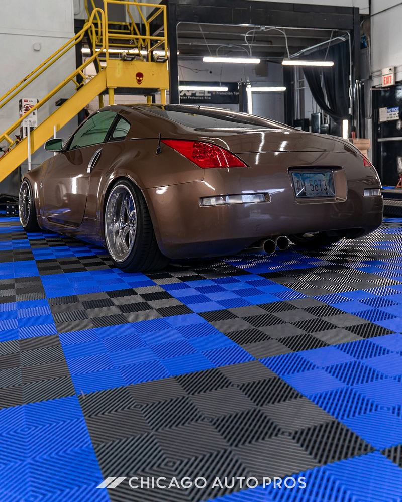 A brown sports car is parked on a checkered floor in a garage.
