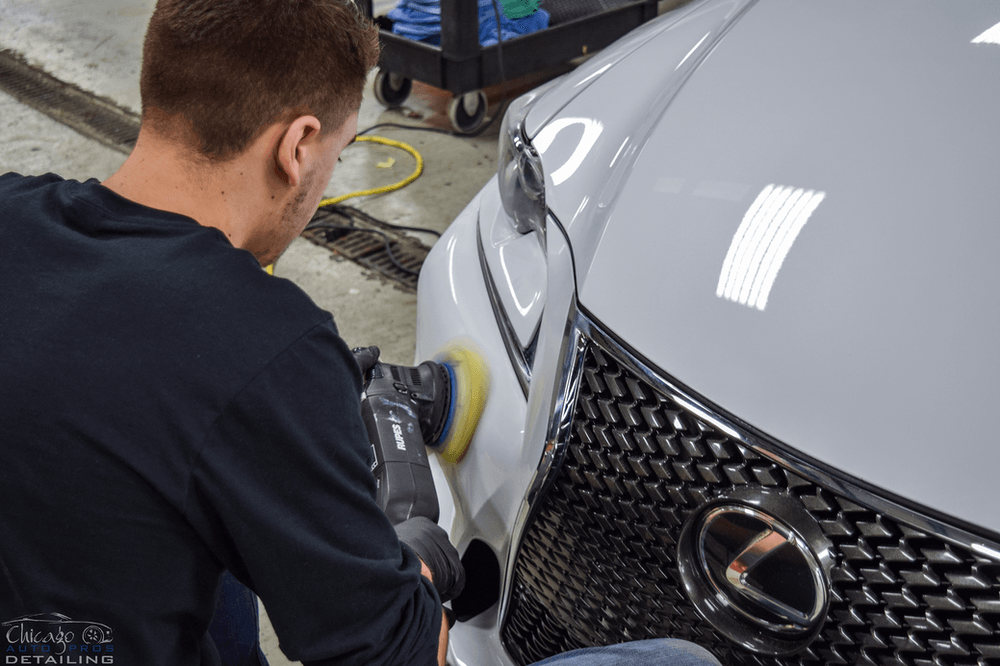 A man is polishing the front of a lexus car.