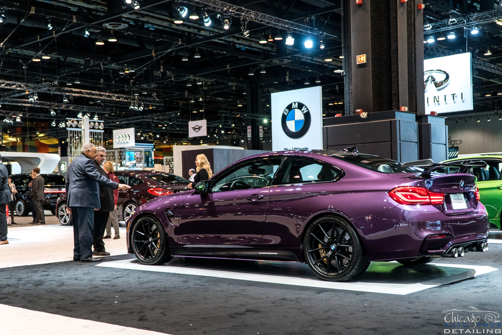 A purple bmw m4 is on display at a car show.