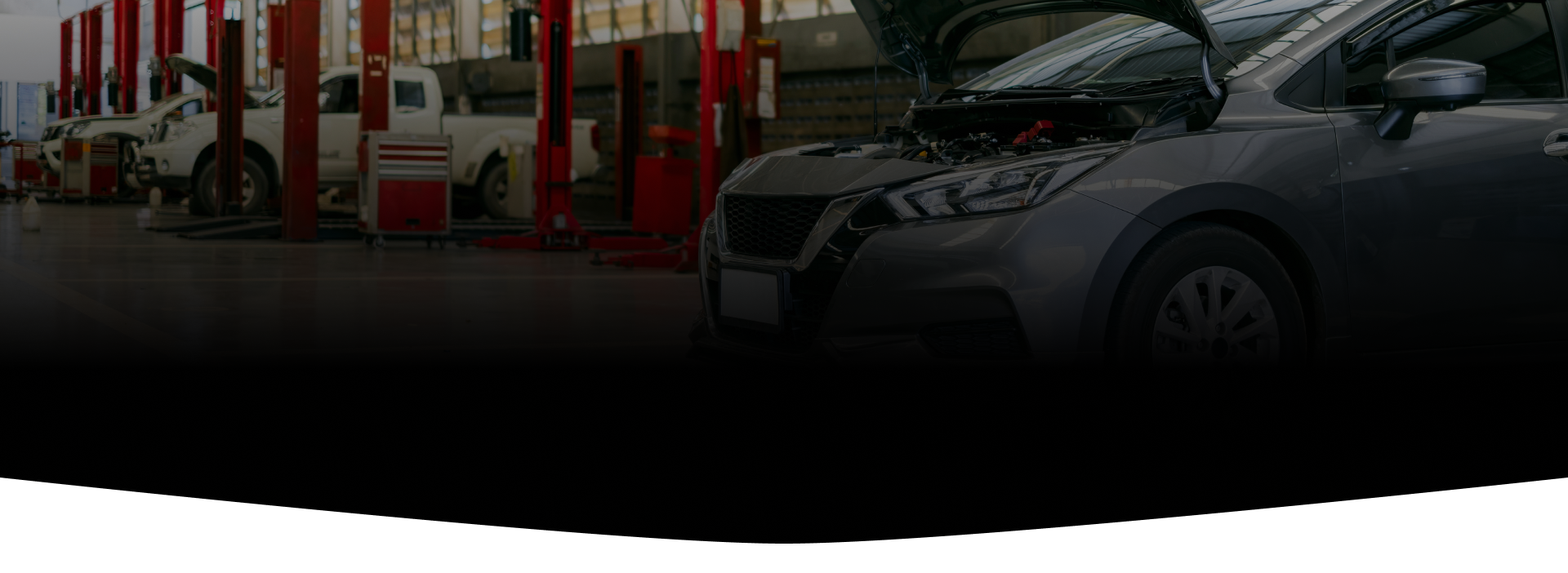 Car in a garage with hood open, other cars and lift equipment visible.