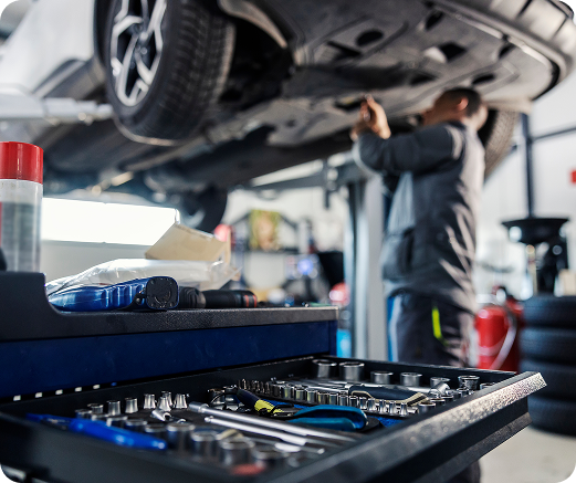 Mechanic working under a car in a garage with a toolbox in the foreground.