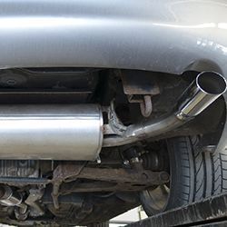 Undercarriage of a silver car, showing exhaust pipe and muffler near a rear tire.